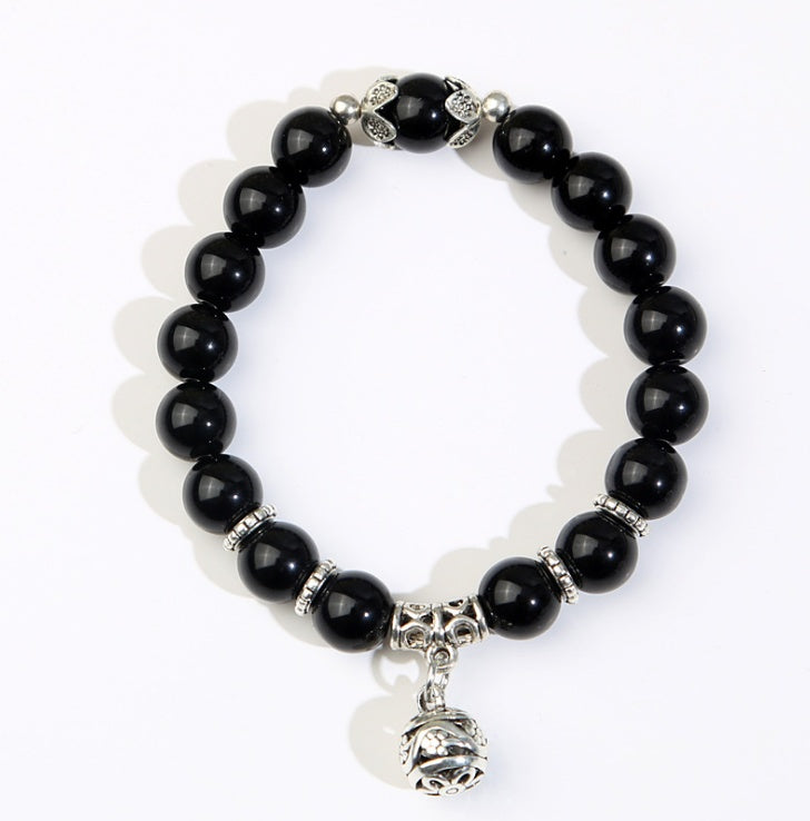 Shadow Guardian obsidian bracelet with glossy black beads, patterned zinc alloy spacers, and a hanging bell charm.