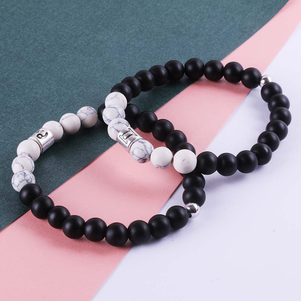 Three beaded bracelets with black, white, and silver beads on a striped background