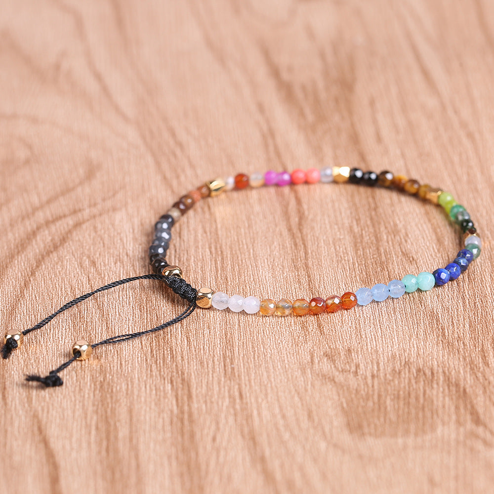 7 chakra bracelet with faceted multicolor agate beads, gold-tone spacers, and black adjustable cord arranged in a circle on a brown wood surface for a clear, detailed product view.