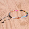 7 chakra bracelet with faceted multicolor agate beads, gold-tone spacers, and black adjustable cord arranged in a circle on a brown wood surface for a clear, detailed product view.
