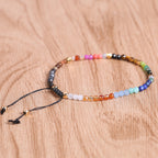 7 chakra bracelet with faceted multicolor agate beads, gold-tone spacers, and black adjustable cord arranged in a circle on a brown wood surface for a clear, detailed product view.