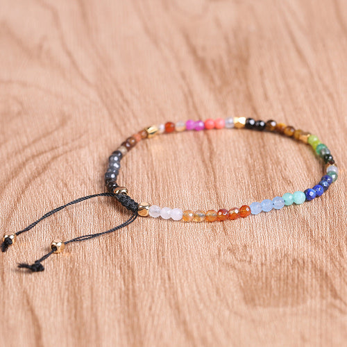 7 chakra bracelet with faceted multicolor agate beads, gold-tone spacers, and black adjustable cord arranged in a circle on a brown wood surface for a clear, detailed product view.