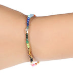 7 chakra bracelet worn on a wrist, showing its slim line of faceted multicolor agate beads, small gold-tone spacers, and black adjustable sliding cord against the white background.