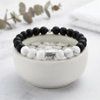 Black and white beaded bracelet with a silver zodiac charm on a white bowl.