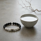 Beaded bracelet with black, white, and silver beads next to a small ceramic bowl on a light gray surface.