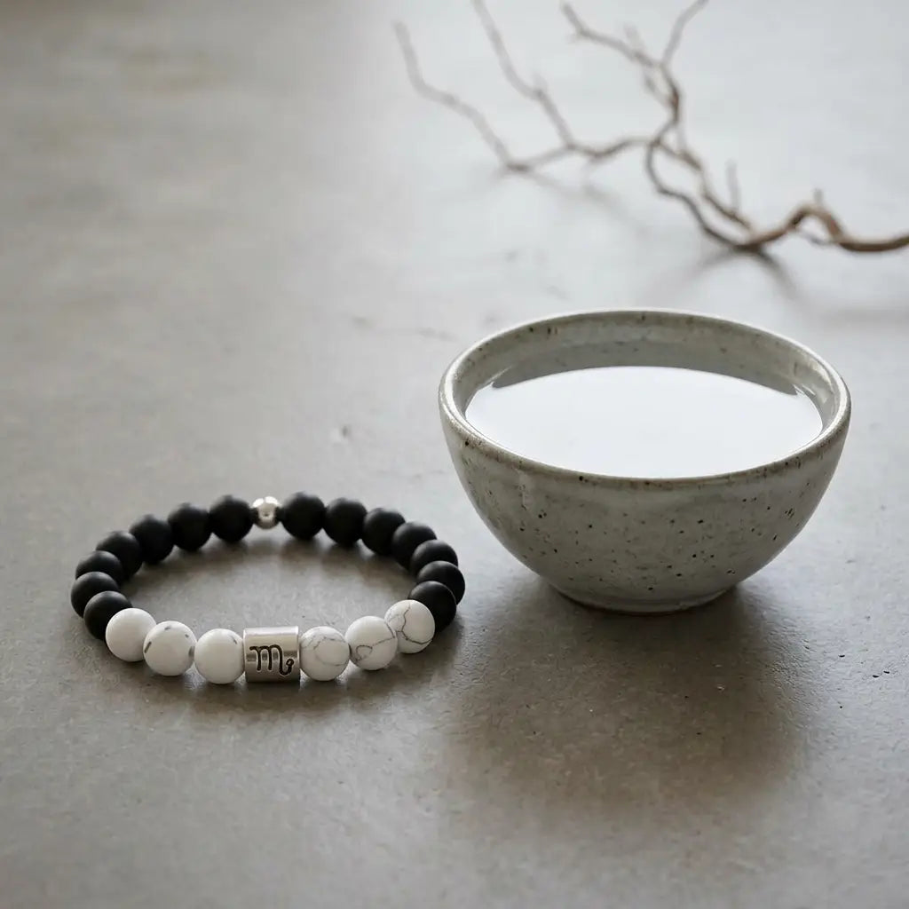 Beaded bracelet with black, white, and silver beads next to a small ceramic bowl on a light gray surface.