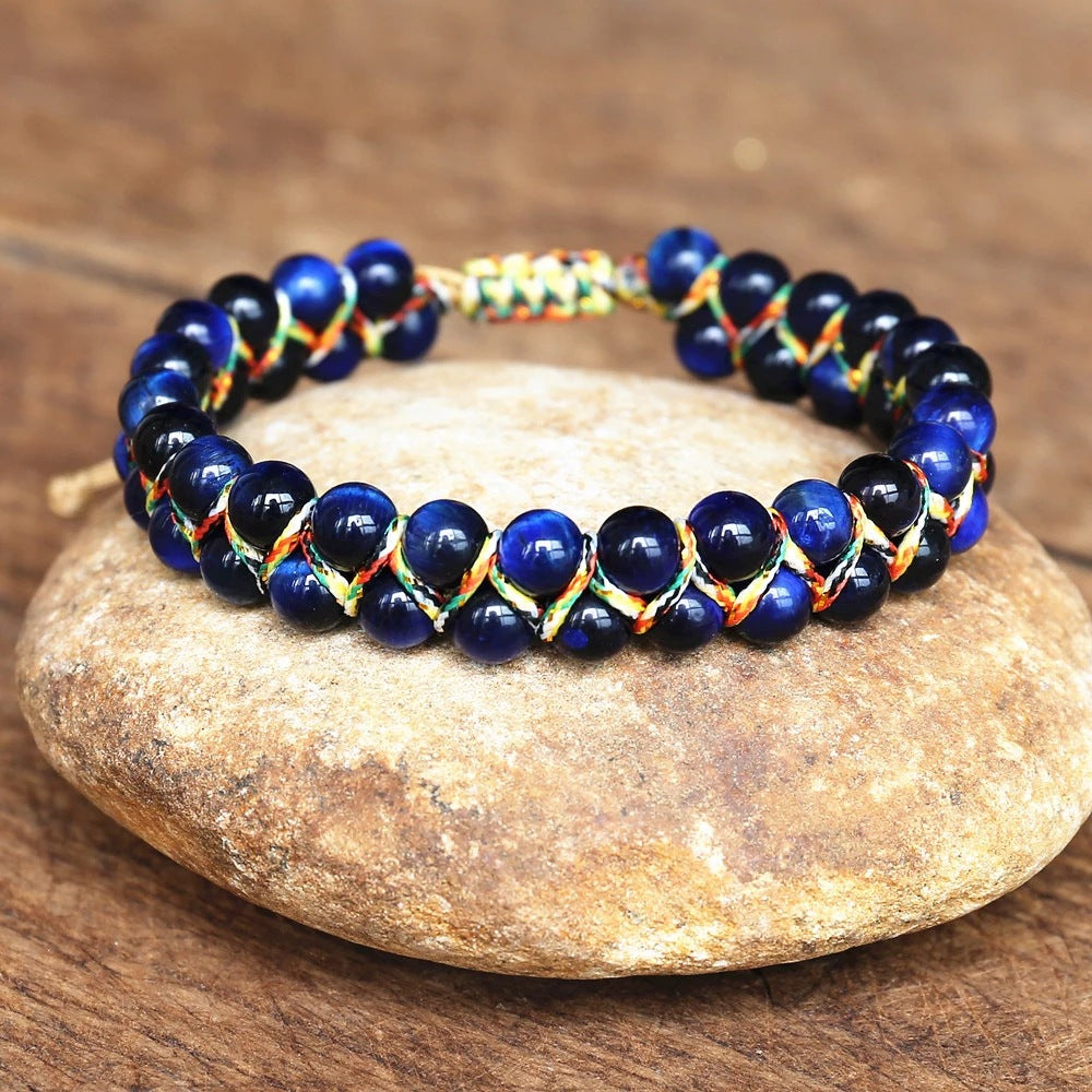 Blue adjustable tiger eye bracelet with glossy round beads, multicolor handwoven cord and sliding closure, displayed on a rustic stone surface for a clear view of the woven design.