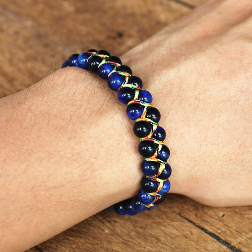 Blue adjustable tiger eye bracelet worn on a wrist, showing glossy round beads, multicolor woven cord and a sliding knot closure for a clear view of the handwoven fit and easy fit.