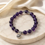 Violet Serenity amethyst bracelet on natural linen with glossy purple beads, showing genuine amethyst color variation, polished stone texture, and a simple everyday bracelet style.