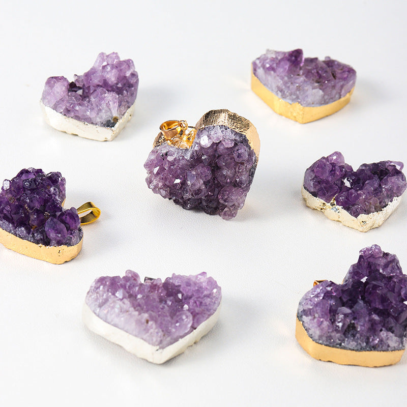 Amethyst heart pendant collection arranged on white with purple crystal clusters, rough sparkling points, varied heart shapes, and gold- or silver-color edging, and bails together.