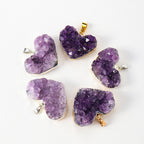 Amethyst heart pendant group with pale to deep purple crystal points irregular cluster texture, heart silhouettes, and mixed gold- and silver-color edging on a clean white display.