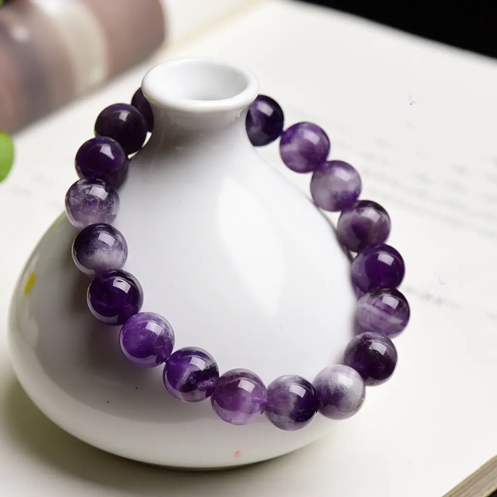 Amethyst jewelry healing crystal bracelet draped over ceramic vase with polished gemstone beads for stylish spiritual decor
