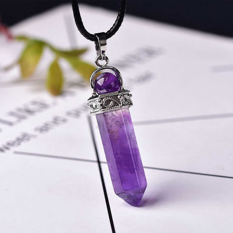 Amethyst point necklace with a polished purple six-sided crystal pendant, round purple accent bead, decorative silver-color cap, and black cord on a soft neutral studio background.