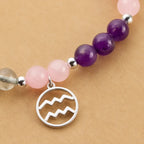 Aquarius stone bracelet closeup featuring silver zodiac pendant with rose quartz and amethyst healing crystal beads.