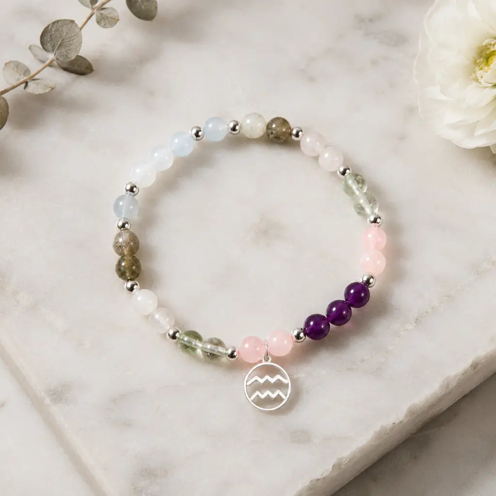 Aquarius stone bracelet on white marble with pastel crystal beads and zodiac charm for elegant astrology fashion.