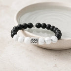Aquarius zodiac bracelet leaning on ceramic bowl with onyx, howlite, and silver charm for premium astro gifting