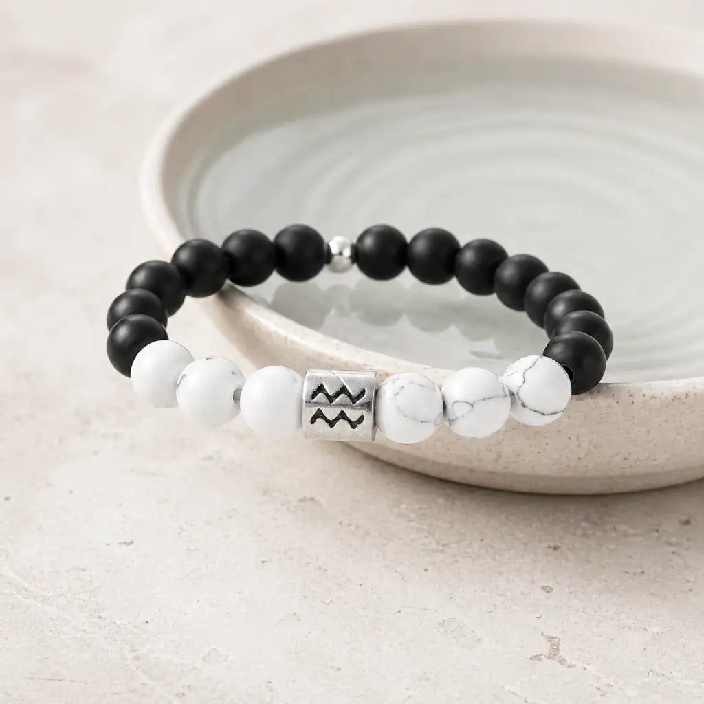 Aquarius zodiac bracelet leaning on ceramic bowl with onyx, howlite, and silver charm for premium astro gifting