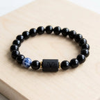 Aries zodiac bracelet on light wood with polished black beads, blue stone accent, and clean everyday style appeal