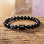 Aries zodiac bracelet on rustic wood with black beads, blue gem accent, and warm spiritual charm for mindful gifting
