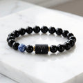 Aries zodiac bracelet on white marble with black beads, blue gem accent, and sleek modern gifting style appeal