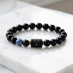 Aries zodiac bracelet on white marble with black beads, blue gem accent, and sleek modern gifting style appeal