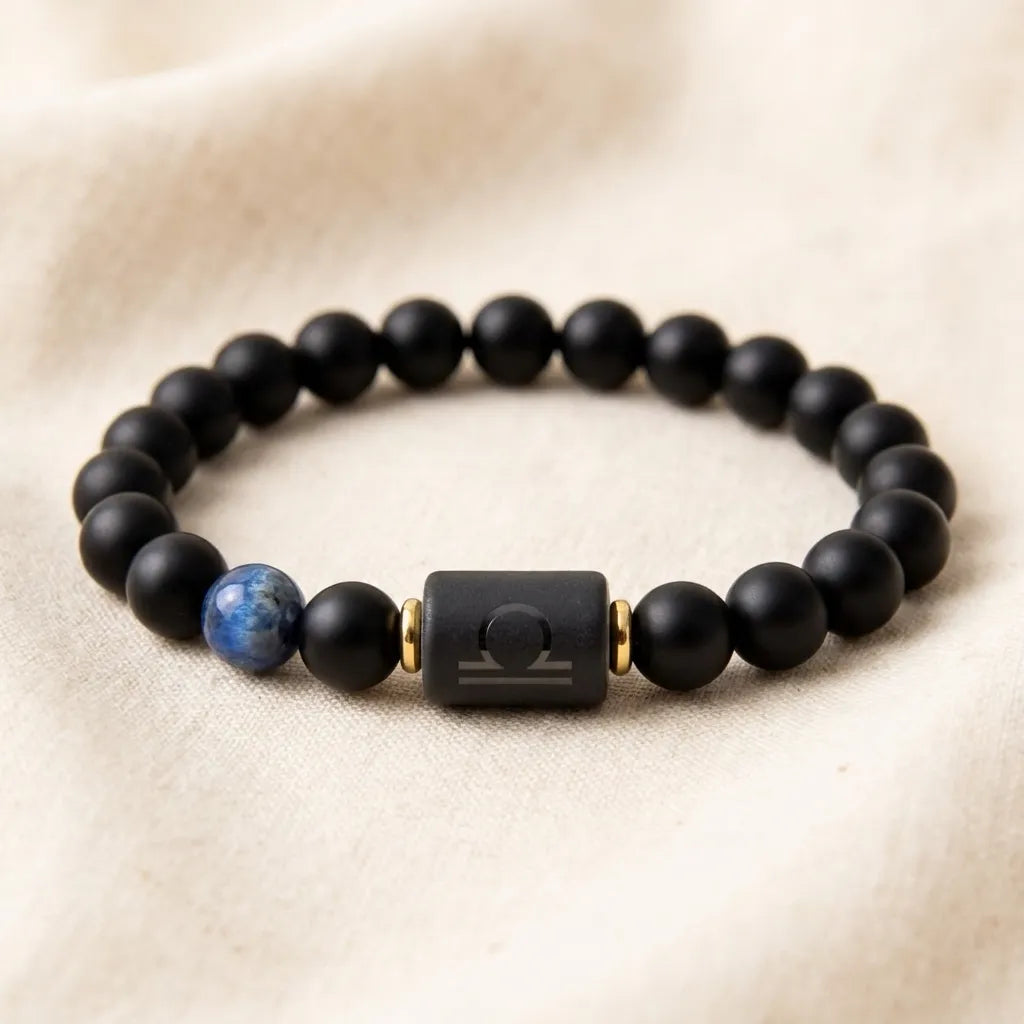 Libra zodiac bracelet with matte black beads, blue accent stone, and engraved center bead on soft cream fabric.