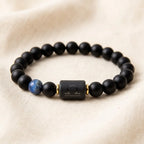 Libra zodiac bracelet with matte black beads, blue accent stone, and engraved center bead on soft cream fabric.