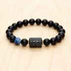 Libra zodiac bracelet with matte black beads, blue accent stone, and engraved center bead on a light wooden surface.