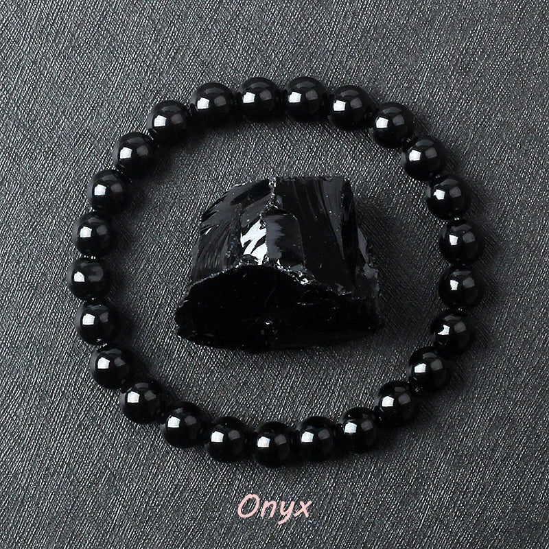 Black onyx bracelet with glossy round beads circling a rough black onyx stone on dark gray fabric, offered in 6 mm and 8 mm sizes plus three wrist lengths on a smooth stretch cord.