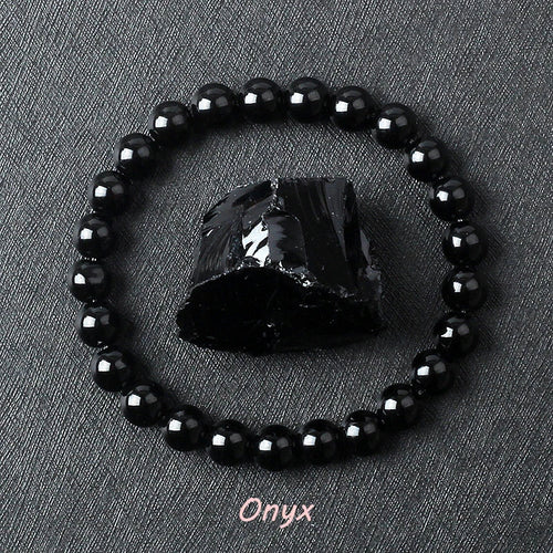 Black onyx bracelet with glossy round beads circling a rough black onyx stone on dark gray fabric, offered in 6 mm and 8 mm sizes plus three wrist lengths on a smooth stretch cord.