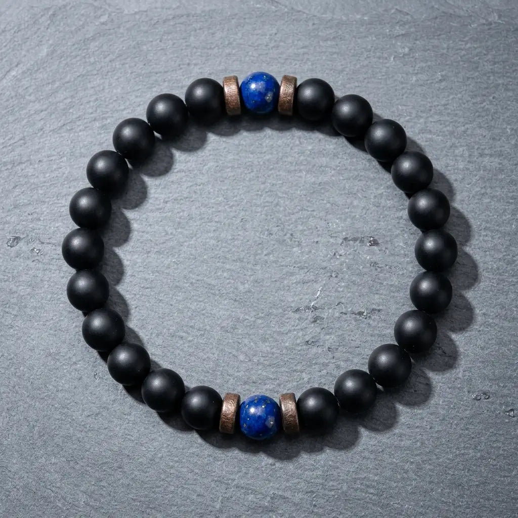 Matte black onyx bracelet with dual lapis lazuli blue beads laid flat on dark grey slate, best natural crystal gemstone bracelet 2026