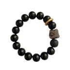 Black stone bracelet flat lay with 12mm glossy round beads, smoky gray patterns, one porous accent bead, a carved lion-style focal, and a thick gold-colored ring detail from above.