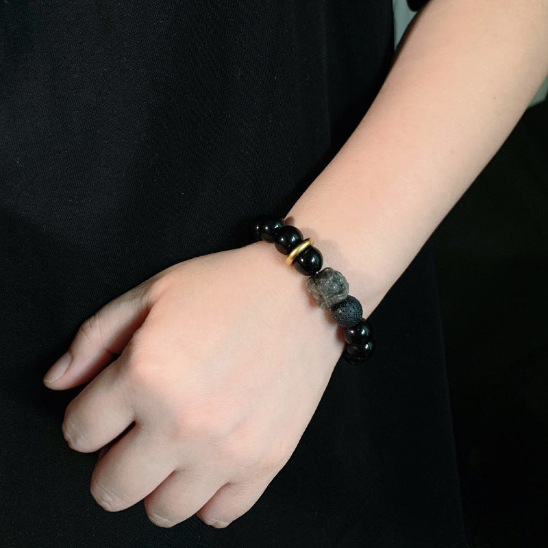 Black stone bracelet on a wrist with glossy round 12mm beads, smoky gray patterns, a carved lion-style focal bead, porous black accent bead and a gold-colored ring shown in detail.