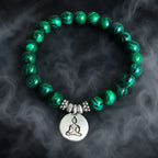 Buddha green tigereye beaded bracelet with silver charm and swirled malachite-style beads on dark background