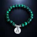 Buddha green tigereye healing stone bracelet with silver charm, deep green swirled beads on dark glowing surface