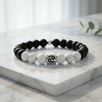 Black and white beaded bracelet with a silver charm on a marble surface