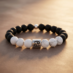 Black and white beaded bracelet with a silver charm on a textured surface