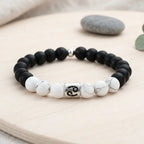Black and white beaded bracelet with a silver charm on a wooden surface.
