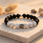 Black and white beaded bracelet with a silver charm on a sandy surface