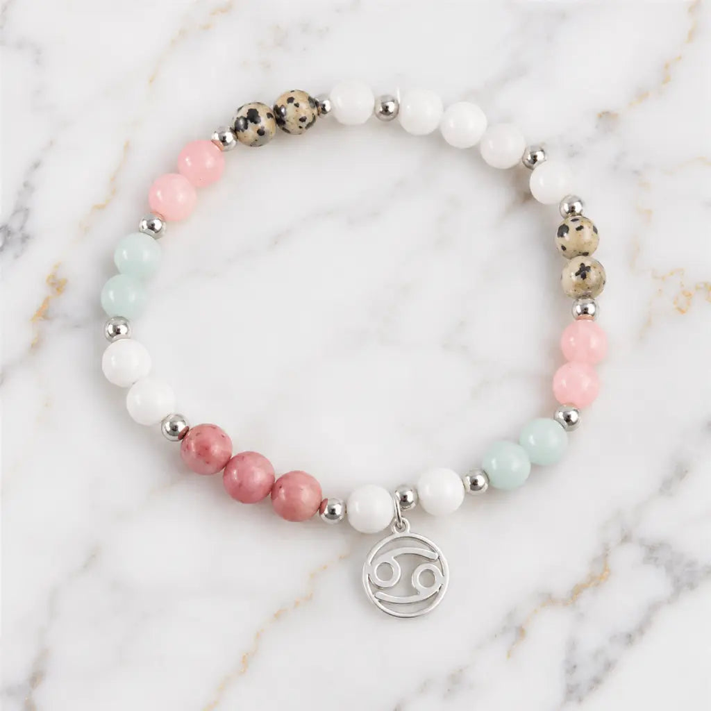 Cancer bracelet flat lay with pastel gemstones silver accents and zodiac charm on elegant marble background