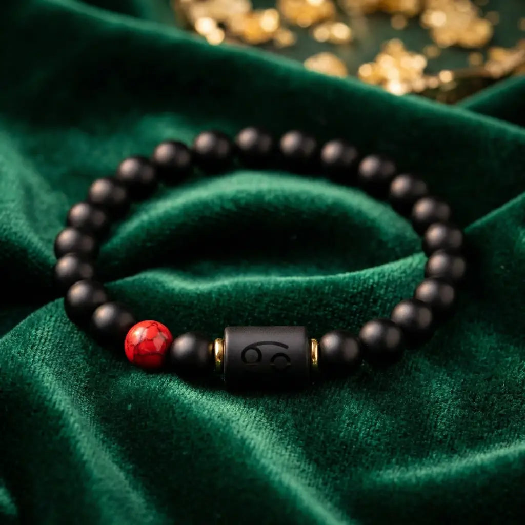 Cancer zodiac Black beaded bracelet with a red bead and gold accent on a green fabric background