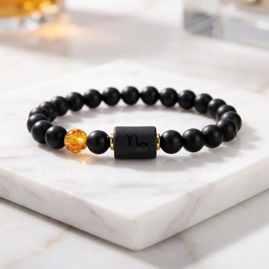 Capricorn zodiac bracelet on marble surface with black beads and amber charm, showcasing premium minimalist jewelry design