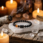Capricorn zodiac bracelet with black beads and amber charm on crystal slab, surrounded by candles for calming ritual energy