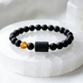 Capricorn zodiac bracelet displayed on white crystal base, black beads and amber accent emphasize clean modern jewelry design