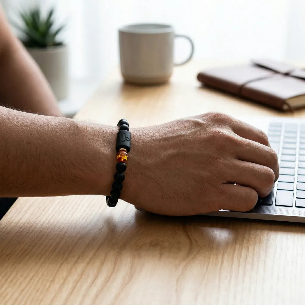 Capricorn zodiac bracelet worn at a laptop with black beads and amber charm for polished everyday confidence