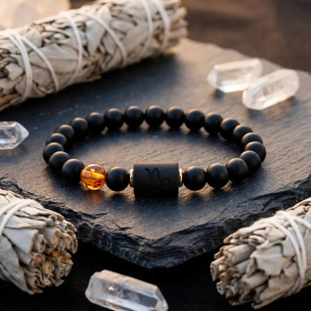 Capricorn zodiac bracelet on stone with sage bundles and crystals, black beads and amber charm highlight grounding energy benefits