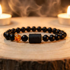 Capricorn zodiac bracelet with black beads and amber charm near candles and smoke, enhancing calming spiritual ritual energy