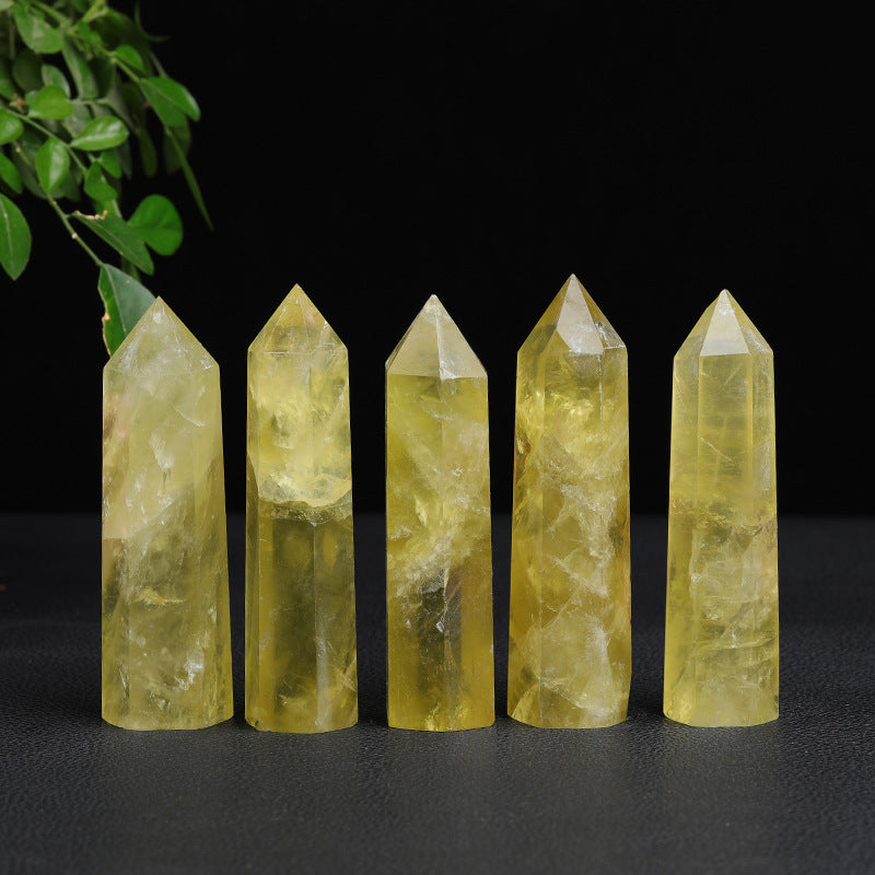 Citrine crystal tower set of five polished yellow points in varied heights, lined up on a black surface with green leaves above, and visible natural-looking inner marks on display.