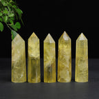 Citrine crystal tower set of five polished yellow points in varied heights, lined up on a black surface with green leaves above, and visible natural-looking inner marks on display.