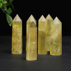 Citrine crystal tower group, with polished hexagonal sides, pointed tops, and yellow quartz tones arranged on a black surface with green leaves in the upper-left corner on display.